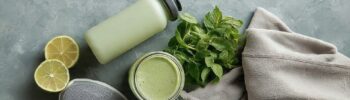 Flat lay d'une gourde, de chaussures de sport, d'un smoothie vert et d'une serviette, illustrant une routine sportive durable.